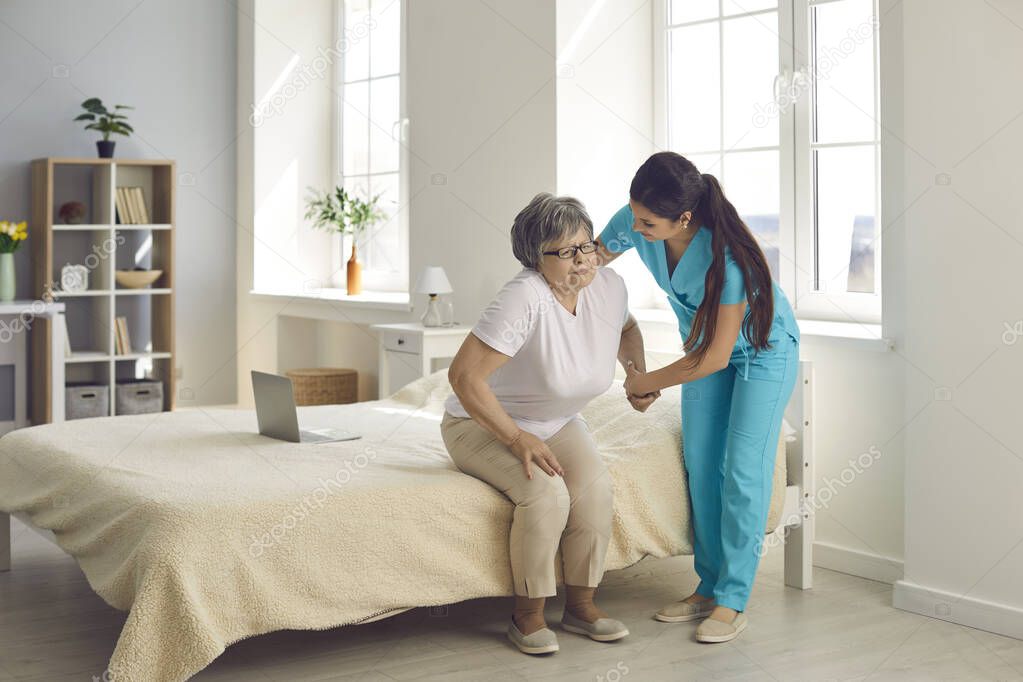 Female caregiver who cares for an elderly woman in a nursing home helps her get out of bed.