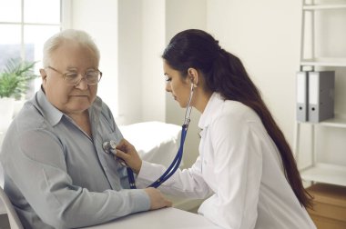 Doktor hastane koğuşunda steteskopla emekli bir adamın ciğerlerini kontrol ediyor.