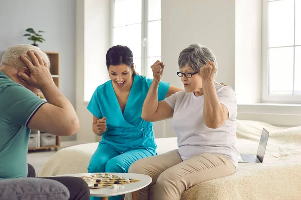 Heureux retraités patients âgés avec infirmière jouer dames et avoir du plaisir — Photo