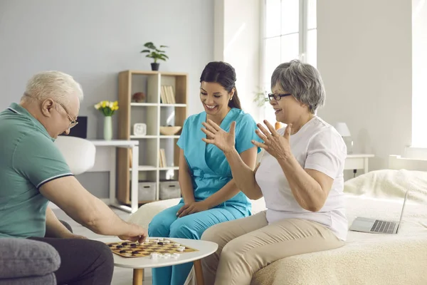 Heureux couple de personnes âgées à la retraite et leur infirmière jouer aux dames et s'amuser ensemble — Photo