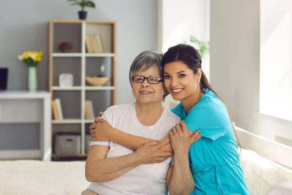 Felice donna anziana insieme con la sua infermiera a casa cura o caregiver sorridente alla macchina fotografica — Foto Stock