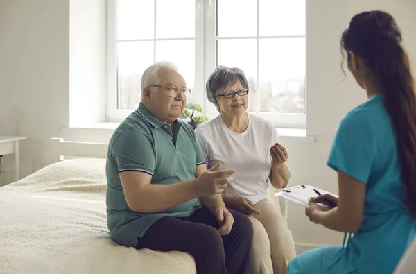 Couple âgé inquiet assis sur le lit et parlant à une infirmière ou à un médecin de famille — Photo