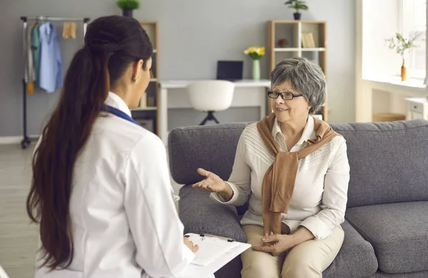 Heureuse femme mature assise sur un canapé à la maison et parlant à son médecin de famille — Photo