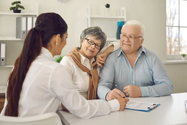 Gelukkige senior paar praten met huisarts zitten aan tafel bij artsen kantoor — Stockfoto
