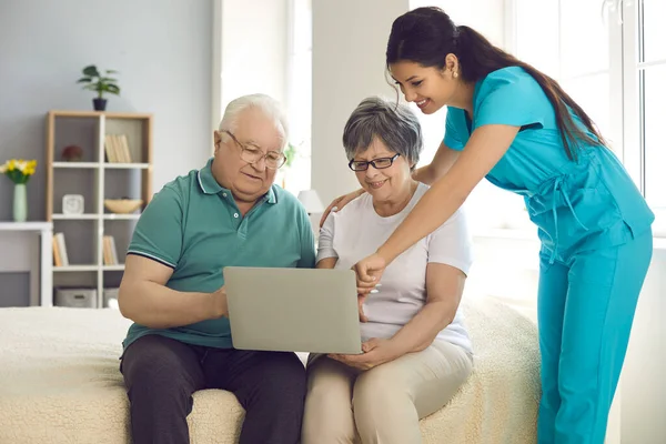 Infermiera domiciliare insegnando ai suoi pazienti anziani felici di utilizzare il computer portatile moderno — Foto Stock