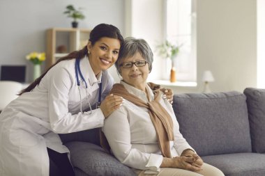 Gülümseyen genç doktor portresi ya da kıdemli hastasını kucaklayan evde bakım hemşiresi.