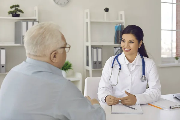 Uśmiechnięta lekarka słuchająca starszego pacjenta podczas rozmowy lekarskiej w jej gabinecie — Zdjęcie stockowe