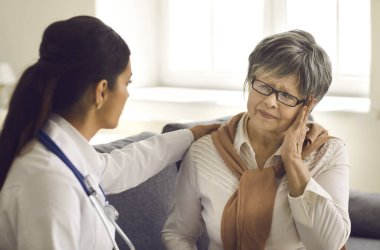 Olgun bir kadın, hastanede sağlık kontrolü sırasında doktoruna baş ağrılarını anlatıyor.