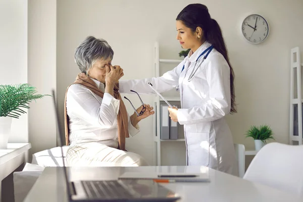 Mulher idosa infeliz com dor de cabeça ou problemas de visão conversando com o médico no hospital — Fotografia de Stock