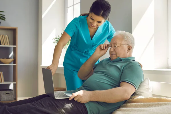 Amicale infirmière souriante montrant vieux patient homme âgé résultat d'analyse sur ordinateur portable — Photo