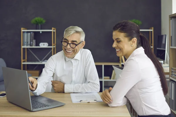 Uśmiechnięty starszy szef i młody pracownik patrzący na ekran laptopa w biurze — Zdjęcie stockowe