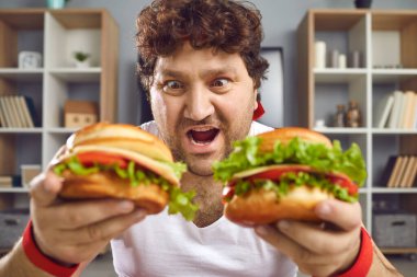 Hungry chubby man looking at two delicious hamburgers with funny face expression