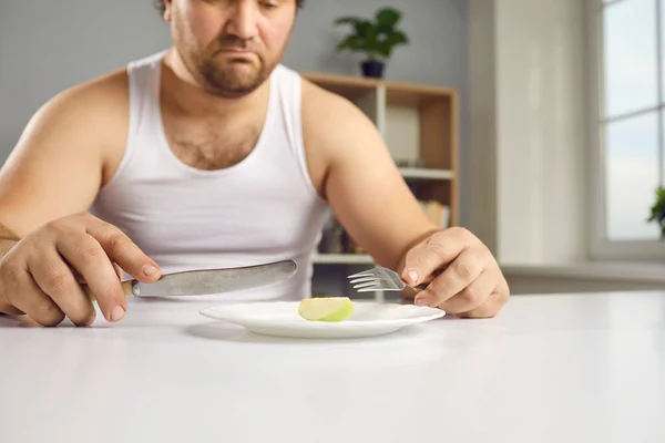 Sad chubby man whos sticking to strict diet looking at tiny piece of apple for lunch — 图库照片