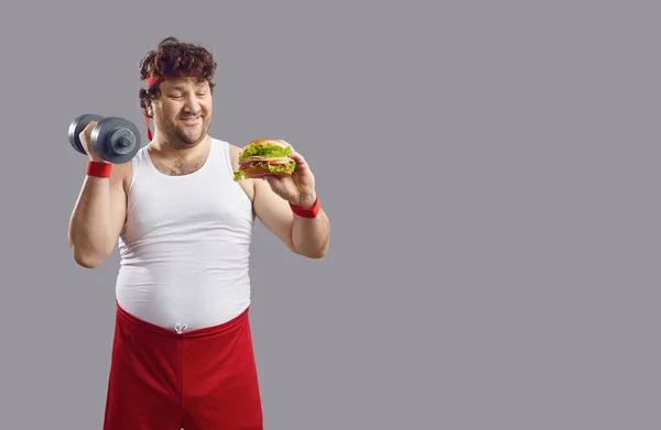 Funny comic overweight man with dumbbell and hamburger isolated studio portrait — Fotografie, imagine de stoc