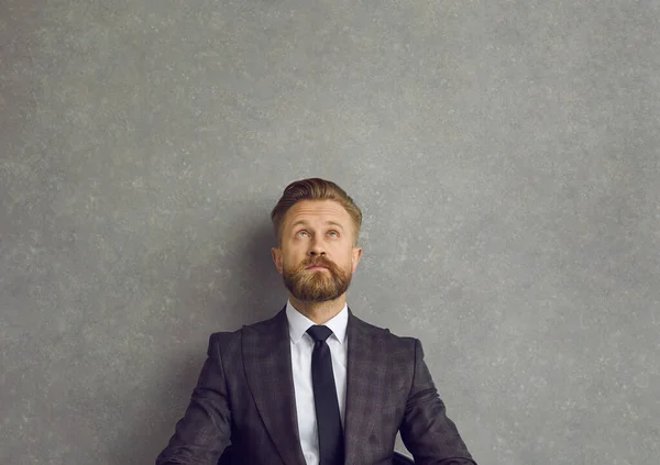 Businessman looking up a at grey copy space wall and thinking of a new business idea — Stockfoto