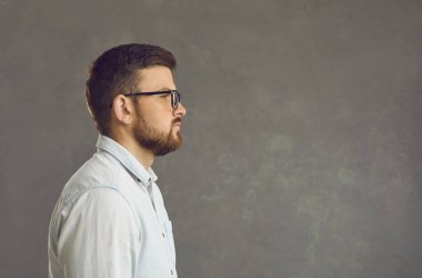 Gri arka planda kendine güvenen genç bir adamın yan görünüm portresi.