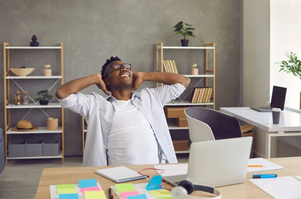 Heureux homme d'affaires afro-américain souriant avec les mains derrière la tête assis au bureau — Photo