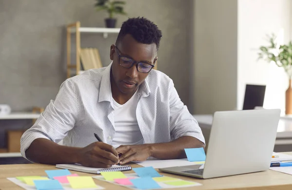 Young handsome minded black businessman writing down ideas in notebook