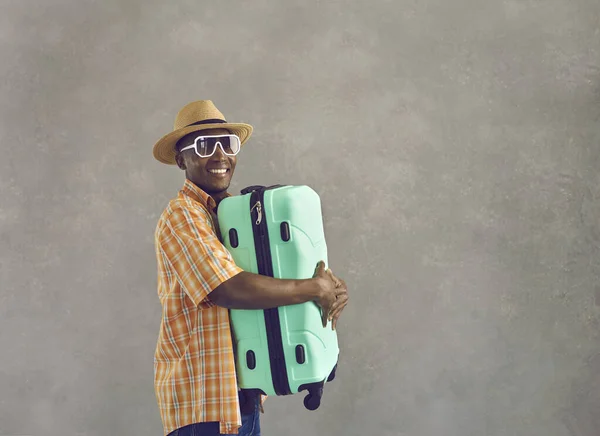 Portrait of happy African man in sunglasses and sun hat holding mint green suitcase — Stock Photo, Image