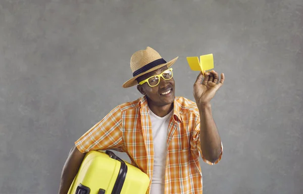 회색 배경에 고립된 여행 가방 과종 이 비행기를 들고 있는 행복 한 흑인 관광객의 모습 — 스톡 사진