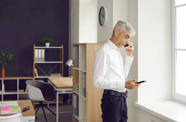 Homme d'affaires mature sérieux parlant téléphone regardant tablette numérique dans le bureau — Photo