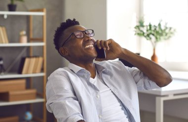 Mutlu siyah iş adamı akıllı telefon tutuyor ve bir arkadaşıyla sohbet ediyor.