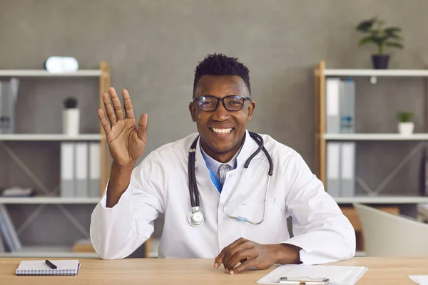 Freundlicher afrikanisch-amerikanischer Arzt winkt Patientin bei Videoanruf mit der Hand. — Stockfoto