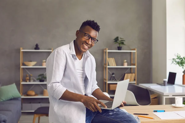 Heureux homme afro-américain intelligent avec ordinateur portable assis sur le bureau regardant la caméra — Photo