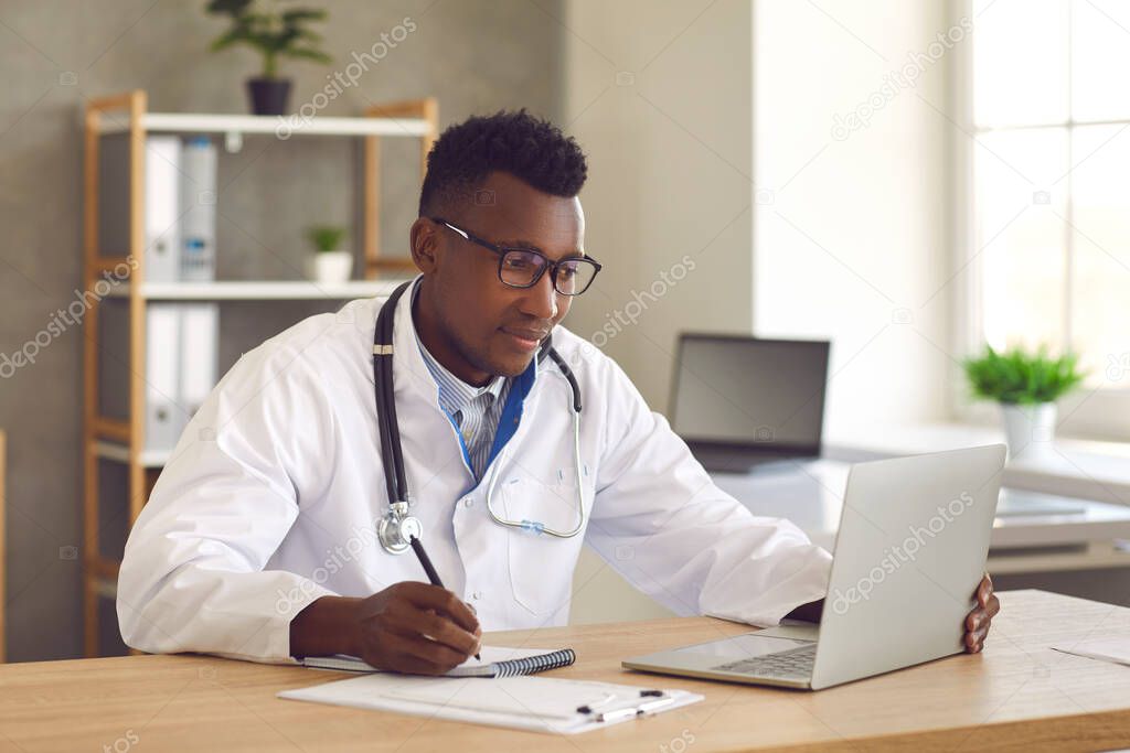 Doctor medical professional looking at laptop screen and writing notes on paper