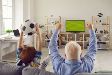 Büyükbabam ve torunum kanepede oturuyor, futbol seyrediyor ve favori takımı destekliyorlar.