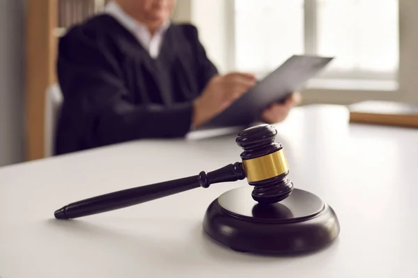 Close-up van een donkerbruine rechter hamer op een tafel tegen de achtergrond van een rechter die een vonnis leest. — Stockfoto