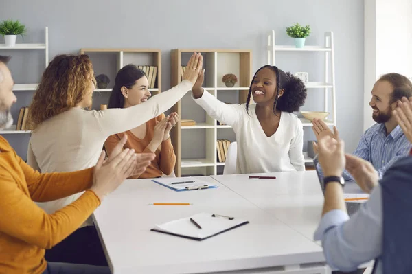 Mulheres de negócios felizes fazendo um acordo e dando cinco pontos altos uns aos outros sentados à mesa em reunião de grupo — Fotografia de Stock