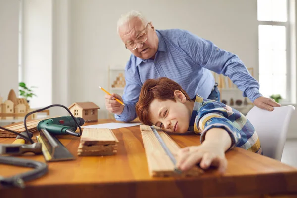 Grand-père et petit-fils mesurant la planche de bois tout en travaillant dans un atelier de menuiserie — Photo