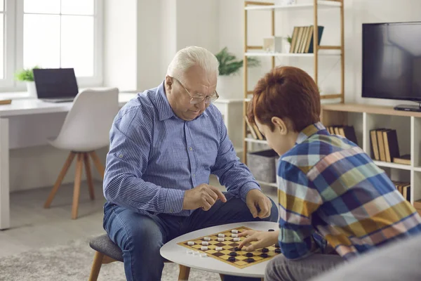 Старший чоловік дідусь сидить і грає в шашки зі своїм онуком — стокове фото