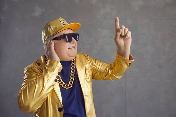 Divertido DJ senior en chaqueta dorada, gorra de béisbol y collar de cadena mezclando música en la fiesta disco —  Fotos de Stock