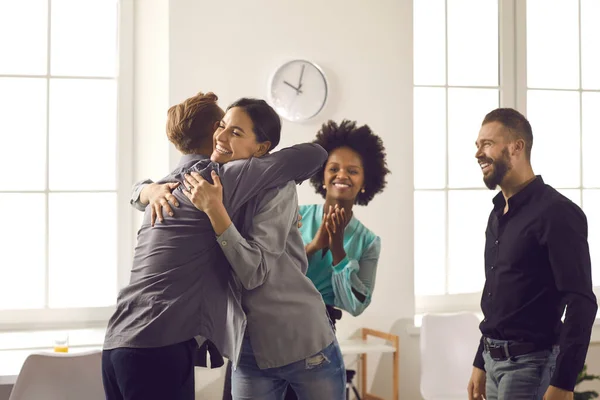 Group of colleagues hugging young man congratulating him on promotion or happy life event