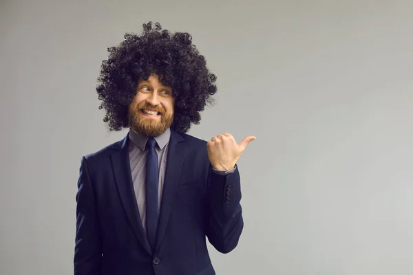 Homem feliz na peruca encaracolado engraçado apontando polegar de distância para publicidade cópia espaço fundo — Fotografia de Stock