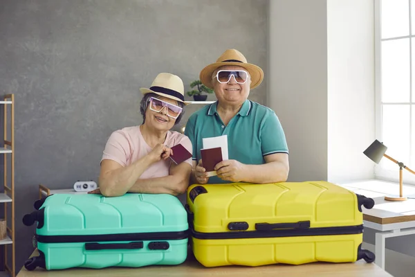 Πορτρέτο του ευτυχισμένου χαριτωμένου ηλικιωμένου ζευγαριού με αεροπορικά εισιτήρια, διαβατήρια και βαλίτσες στο σπίτι — Φωτογραφία Αρχείου