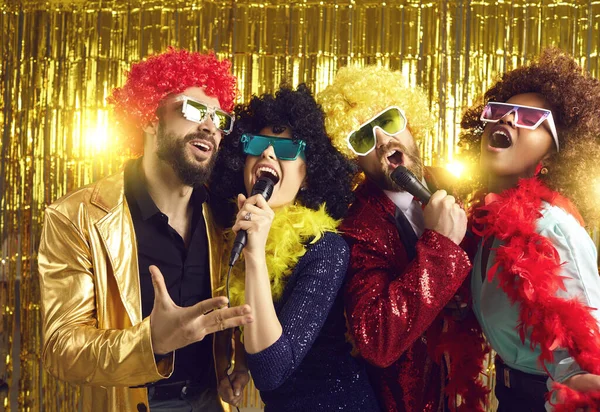 Szczęśliwi rozradowani przyjaciele w zabawnej peruce i kostiumie śpiewający na mikrofonie karaoke — Zdjęcie stockowe