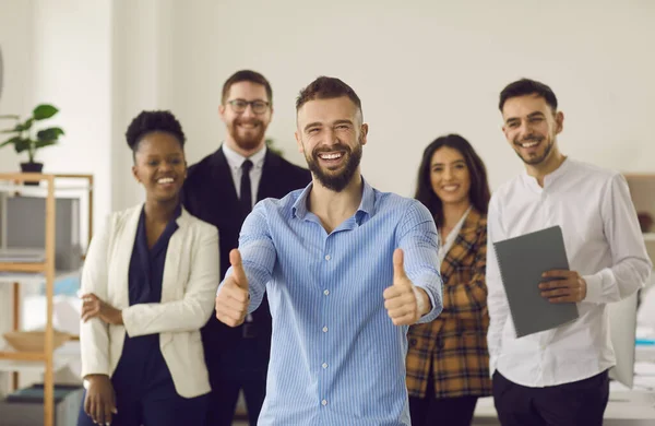 Un leader souriant brandissant les pouces debout avec une équipe d'affaires diversifiée au bureau — Photo