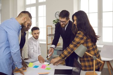 İş dünyası ekibi bir başlangıç projesini tartışırken renkli yapışkan etiketler hakkında notlar yazar.