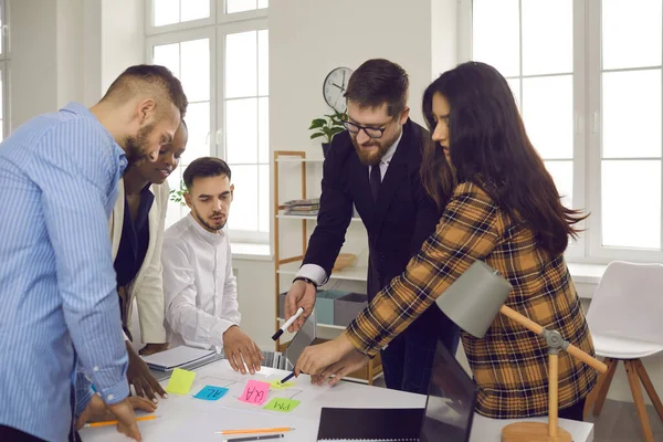 İş dünyası ekibi bir başlangıç projesini tartışırken renkli yapışkan etiketler hakkında notlar yazar.