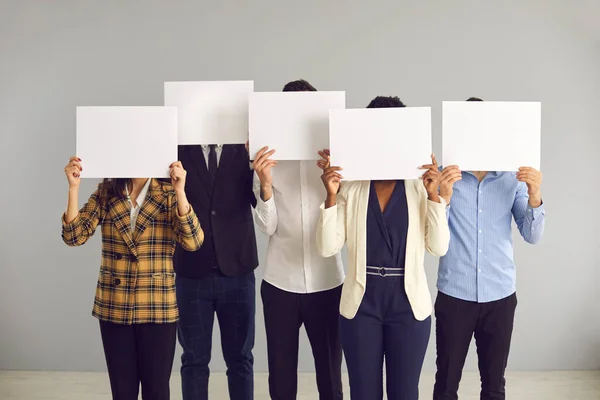 Grupo de personas anónimas cubriendo rostros escondidos detrás de hojas de papel maquetas blancas —  Fotos de Stock