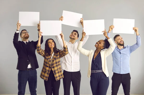 Grupo de personas felices de pie sobre fondo gris y sosteniendo pancartas blancas de maqueta — Foto de Stock