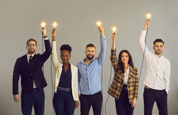Gente creativa de negocios sosteniendo bombillas brillantes de pie sobre fondo gris estudio — Foto de Stock