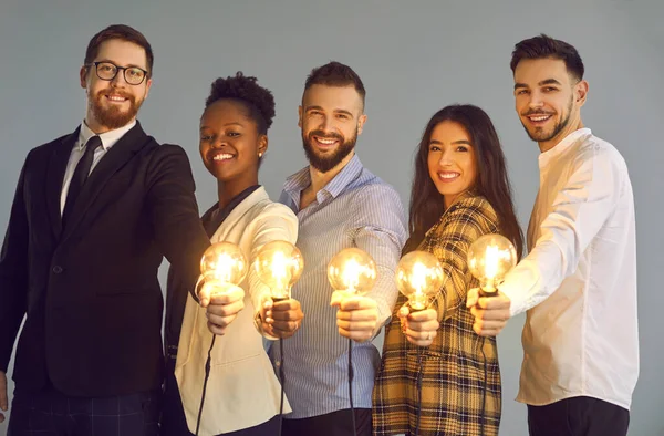 Skupina šťastných mladých různorodých podnikatelů držících zářící žárovky a usmívajících se — Stock fotografie