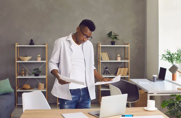 Sérieux homme afro-américain faisant de la paperasse d'affaires et utilisant un ordinateur portable dans son bureau à domicile — Photo