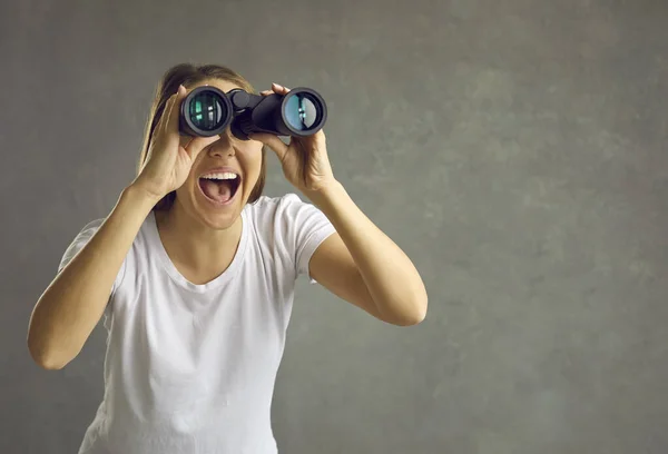 Joven mujer sonriente mirando a través de prismáticos con expresión sorprendida — Foto de Stock