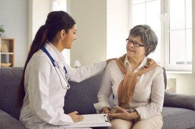 Doktor, ev ziyareti sırasında koltukta oturan kıdemli hastasına güven veriyor.