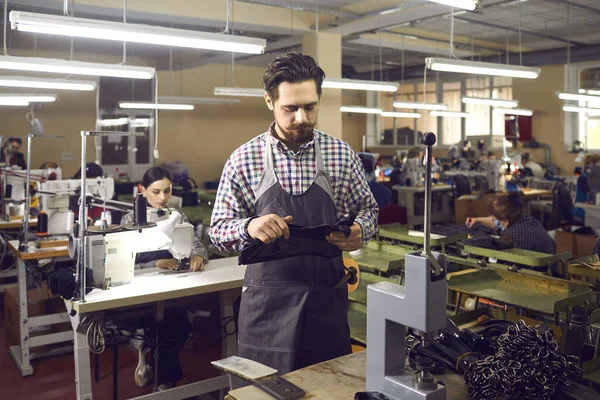 Experienced craftsman working in a leather goods factory is preparing to make new belts.